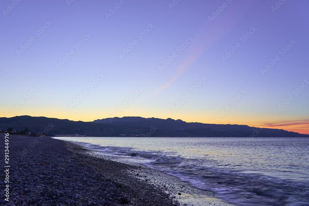 The sunset on the pebble beach with hills on the background, Kolymbari, Crete, Greece.