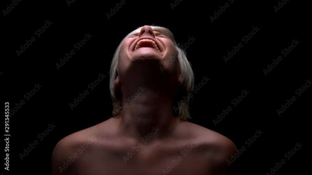 Young blond emotional naked woman screaming in the air. Slow motion shot with black background.