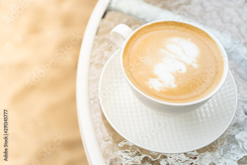 a cup of coffee cappuccino put in white cup places on white plate on a round glass table