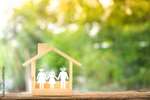 Wooden home with happy family of paper art is placed inside on nature bokeh in the public park, The saving money for house or real estate owner in the future concept.