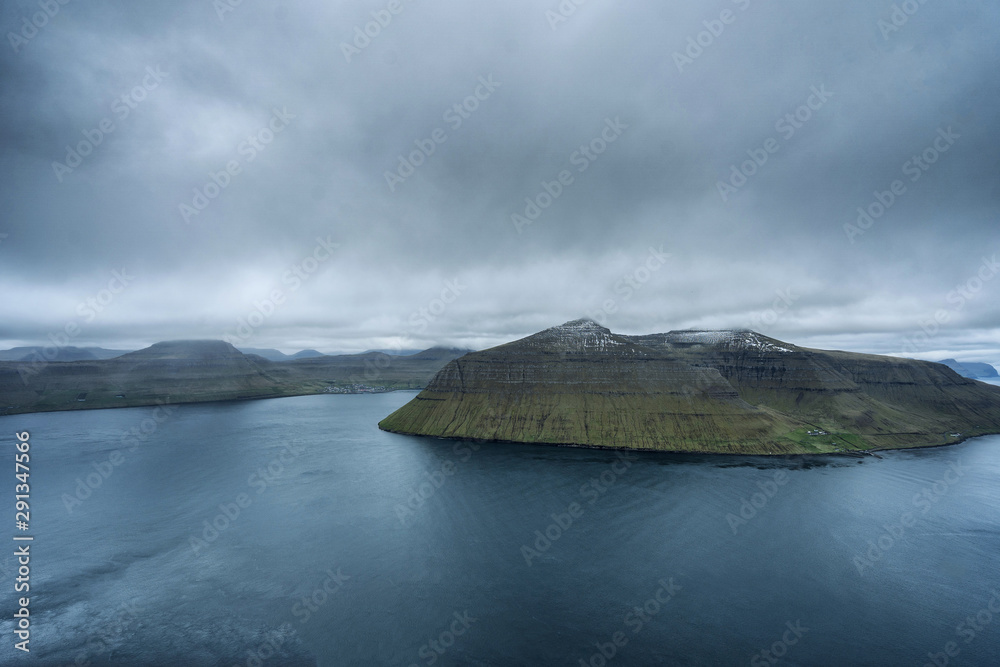 Dramatic landscape of Faroe Islands with grass meadows and rocky cliffs in stormy weather.