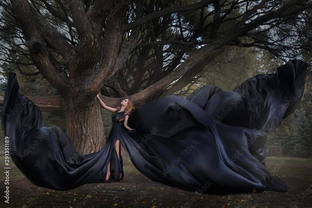 Beautiful girl in a long black flying dress in a mysterious forest.
