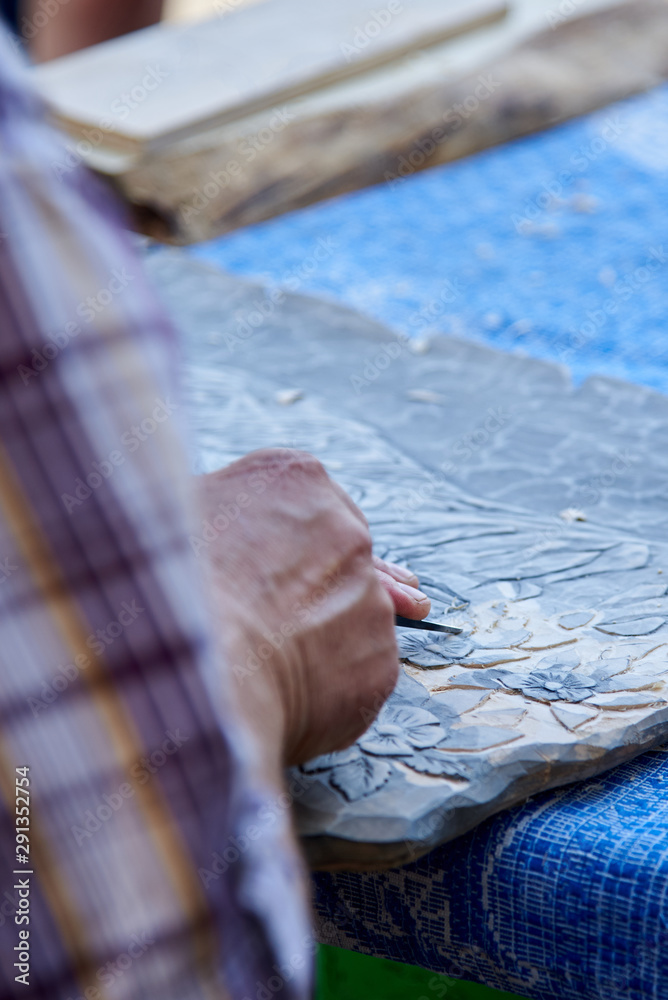 Fototapeta premium Hands of a man carving a picture of wood with a cutter.
