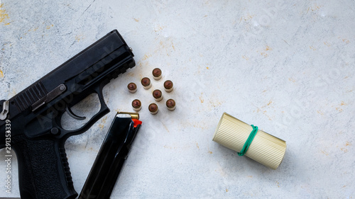 9 mm pistol gun bullets strewn and roll american dollar banknotes on rustic oak table.