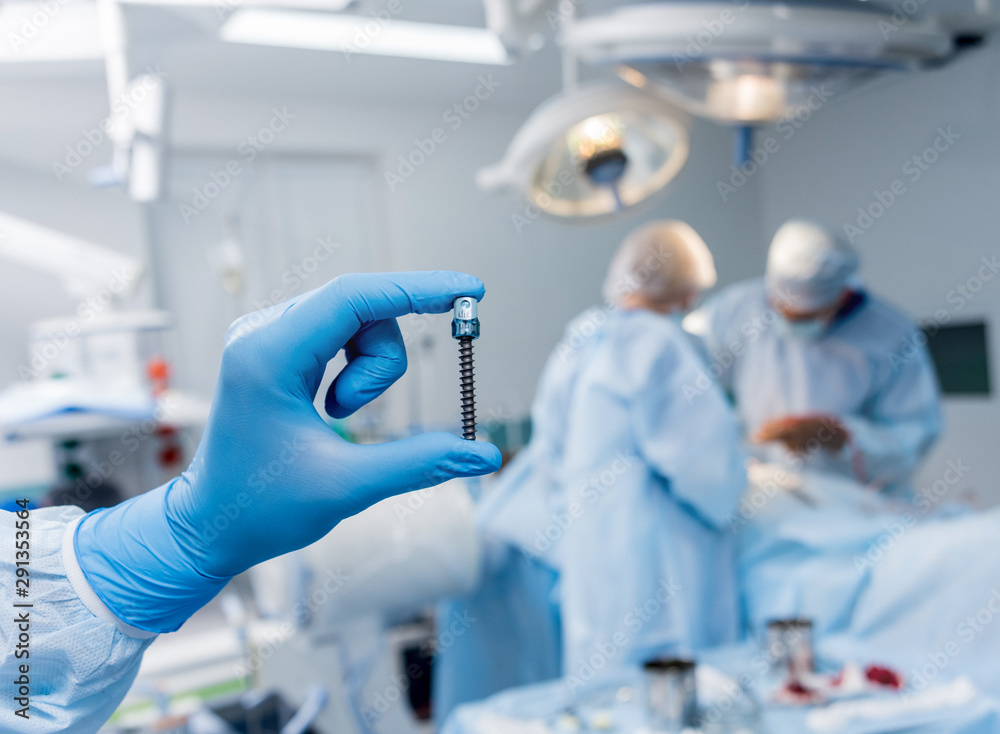 Spinal surgery. Surgeon show polyaxial screw in operating room with surgery equipment. Laminectomy. Spine fixation systems Spinal surgery. Surgeon show polyaxial screw in operating room with surgery equipment. Laminectomy. Spine fixation systems