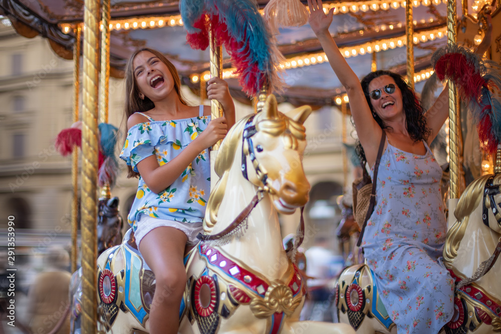 Obraz premium Happy family (mother and daughter) at the carousel. Merry go round horse with colorful lights 