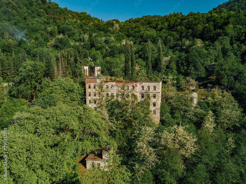 Ruined overgrown school in ghost mining town Akarmara, consequences of war in Abkhazia, aerial view from drone