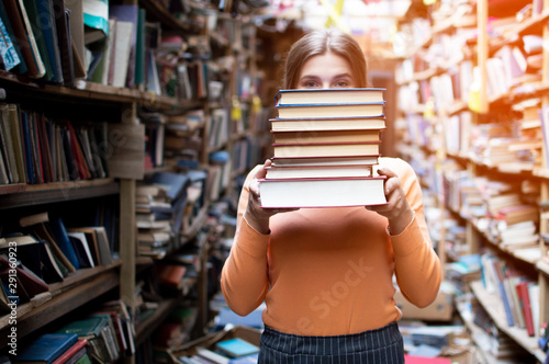girl student holds a stack of books in the library, she searches for literature and offers to read, a woman prepares for study, knowledge is power, bookseller on the background of the bookstore
