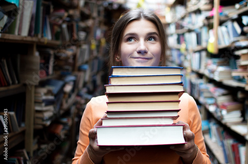 Canvas Print girl student holds a stack of books in the library, she searches for literature