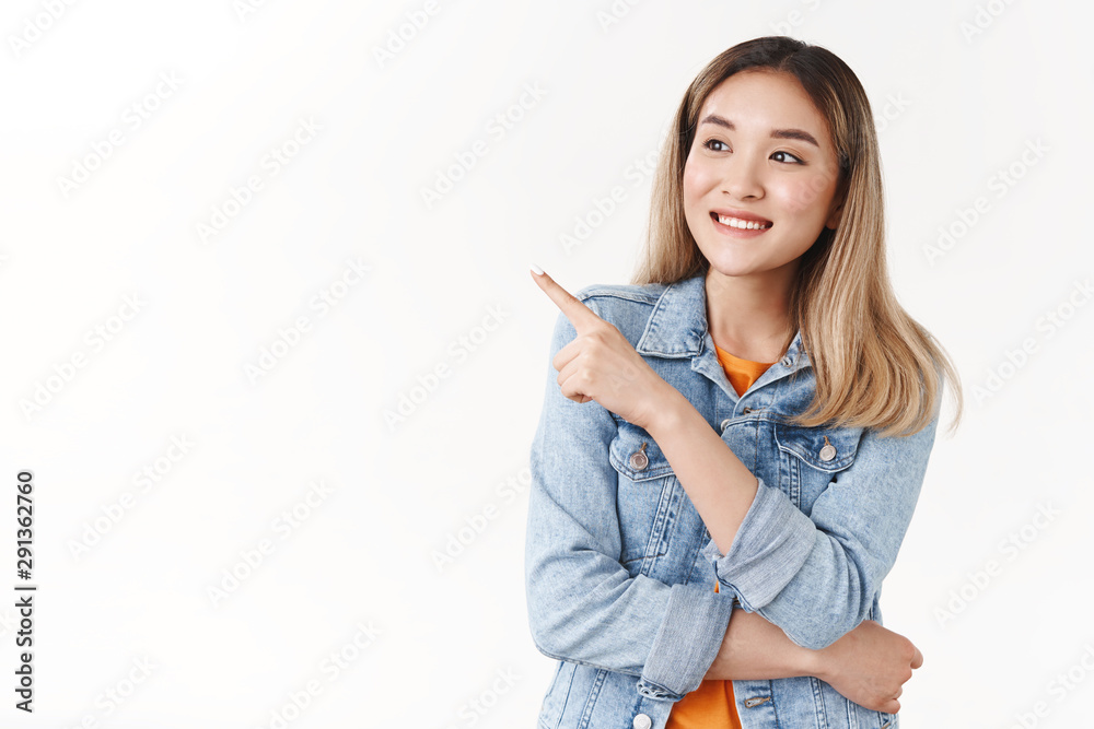 Amused young tender feminine asian blond girl contemplating wonderful scenery pointing looking amazed left directing index finger aside enjoying interesting scene standing white background Amused young tender feminine asian blond girl contemplating wonderful scenery pointing looking amazed left directing index finger aside enjoying interesting scene standing white background