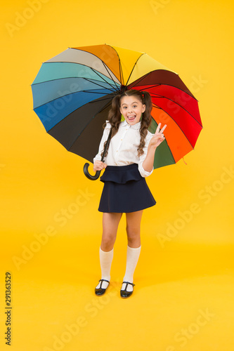 Learning brings you victory. Happy small schoolgirl celebrating victory on yellow background. Little child smiling with victory gesture under colorful umbrella. V is for victory