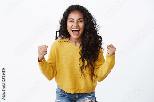 Pretty upbeat african american curly-haired girl in yellow sweater rooting for favorite team, do fist pump say yeah, smiling happily, enjoy watching game in pub, standing white background