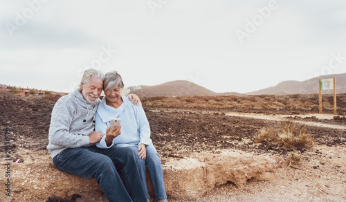 Two senior people sitting and looking at the cell. Hugging and smiling. Morning soon outside, ready for un healthy excursion. Vacation and happiness © luciano