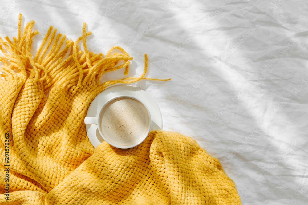 Bedding with a yellow knitted plaid and cup of coffee . Cozy background with copy space. Hygge concept. - obrazy, fototapety, plakaty 