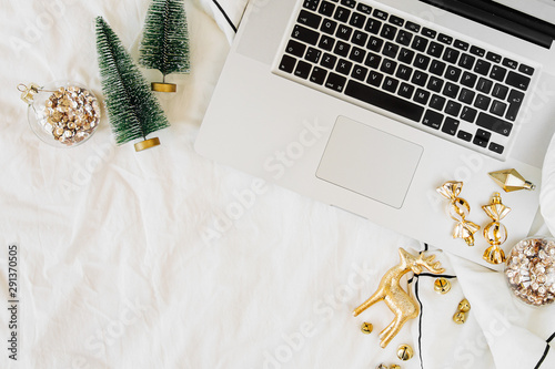 Workspace in bed with laptop and Christmas decorations. Holiday concept. Flat lay, top view
