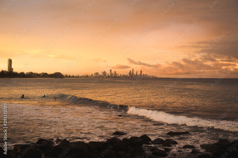 Beautiful sunset over the city while surfers are enjoying the waves