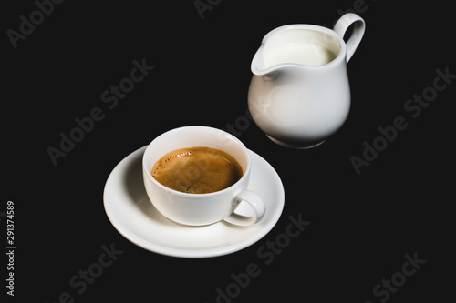 Fotografie White espresso cup with coffee and milk jug on black background