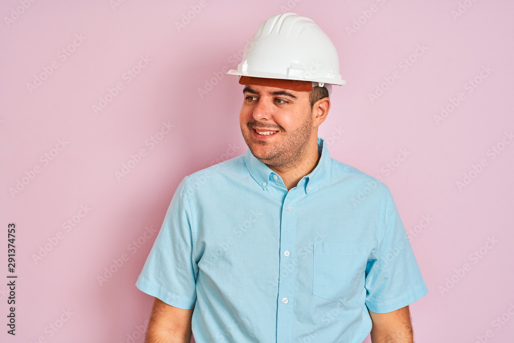 Young architect man wearing security helmet standing over isolated pink background looking away to side with smile on face, natural expression. Laughing confident. Young architect man wearing security helmet standing over isolated pink background looking away to side with smile on face, natural expression. Laughing confident.