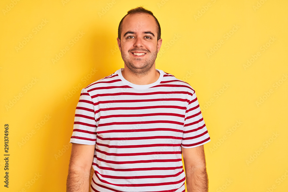 Fototapeta premium Young man wearing casual striped t-shirt standing over isolated yellow background with a happy and cool smile on face. Lucky person.