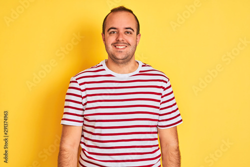 Young man wearing casual striped t-shirt standing over isolated yellow background with a happy and cool smile on face. Lucky person.