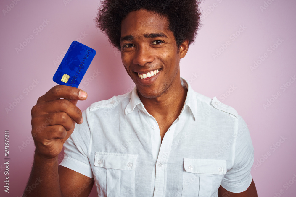 Afro american customer man holding credit card standing over isolated pink background with a happy face standing and smiling with a confident smile showing teeth Afro american customer man holding credit card standing over isolated pink background with a happy face standing and smiling with a confident smile showing teeth
