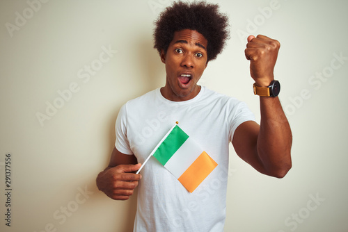 Young african american man holding Ireland Irish flag standing over isolated white background annoyed and frustrated shouting with anger, crazy and yelling with raised hand, anger concept