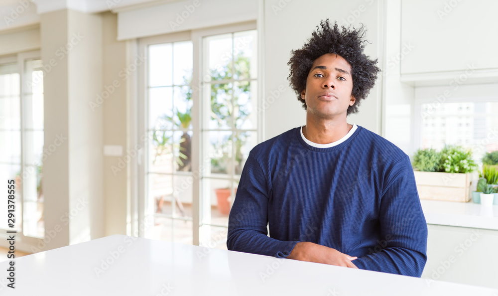 Fototapeta premium Young african american man wearing casual sweater sitting at home Relaxed with serious expression on face. Simple and natural looking at the camera.