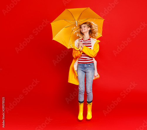 young happy emotional cheerful girl laughing and jumping with yellow umbrella on colored red background.