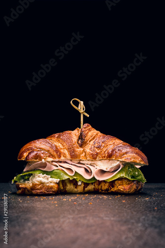 Croissant sandwich with fresh salad, ham and cream cheese on dark background