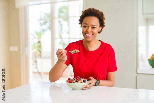 Young beautiful african american woman with afro hair eating healthy wholemeal cereals and berries as healthy breakfast