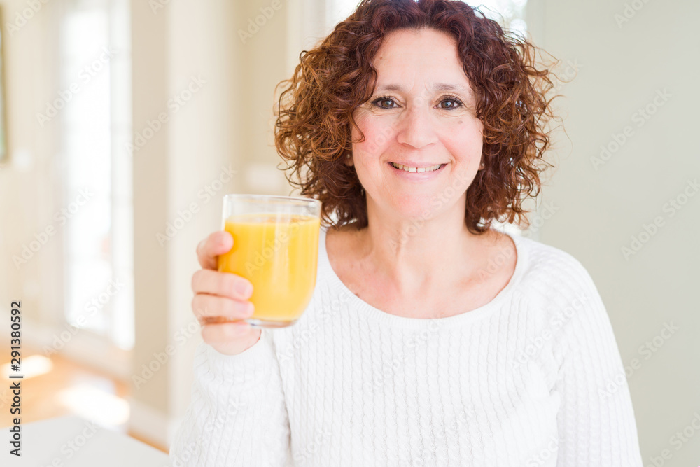 Senior woman driking a glass of fresh orange juice with a happy face standing and smiling with a confident smile showing teeth Senior woman driking a glass of fresh orange juice with a happy face standing and smiling with a confident smile showing teeth
