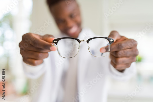 African american optiian man holding and showing glasses lens to custumers at the optics shop while smiling confident