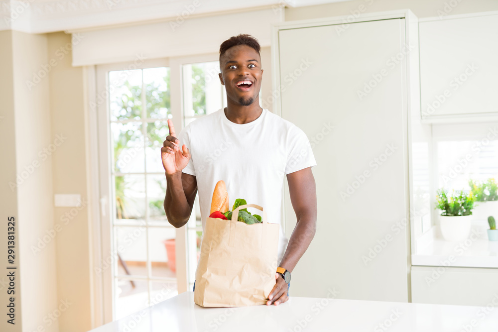 African american man holding paper bag full of fresh groceries surprised with an idea or question pointing finger with happy face, number one