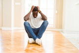 Handsome african american man sitting on the floor at home suffering from headache desperate and stressed because pain and migraine. Hands on head.