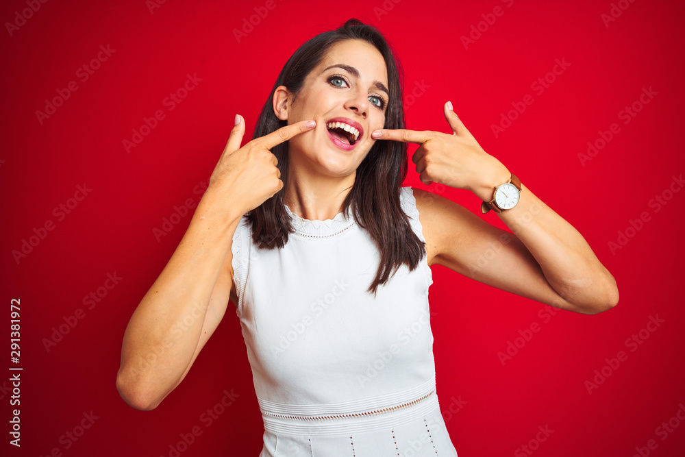 Fototapeta premium Young beautiful woman wearing white dress standing over red isolated background smiling cheerful showing and pointing with fingers teeth and mouth. Dental health concept.