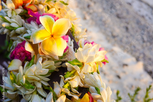 A lei of colorful tropical flowers with a white sandy beach for copy space