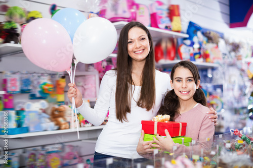 Portrait of mother and daughter holding gifts and balloons in store