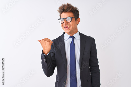 Young handsome businessman wearing suit and glasses over isolated white background smiling with happy face looking and pointing to the side with thumb up.