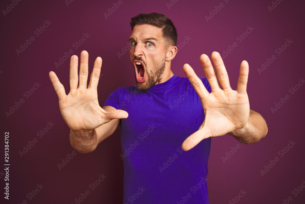 Young man wearing casual purple t-shirt over lilac isolated background afraid and terrified with fear expression stop gesture with hands, shouting in shock. Panic concept. Young man wearing casual purple t-shirt over lilac isolated background afraid and terrified with fear expression stop gesture with hands, shouting in shock. Panic concept.