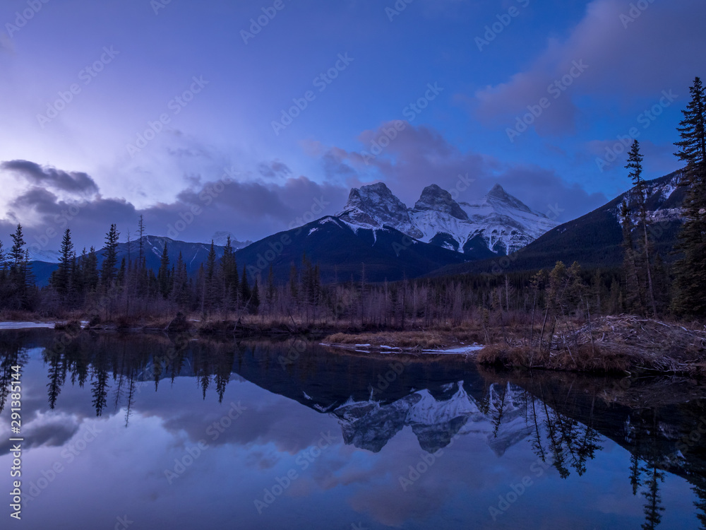 Sunrise view of Policeman`s Creek along the Bow River outside Canmore, Alberta in winter. Pictured is the famous mountain known as the Three Sisters.