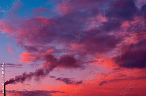 smoking chimney of a factory against fiery orange sunset. colorful and speckled clouds. © Lumppini