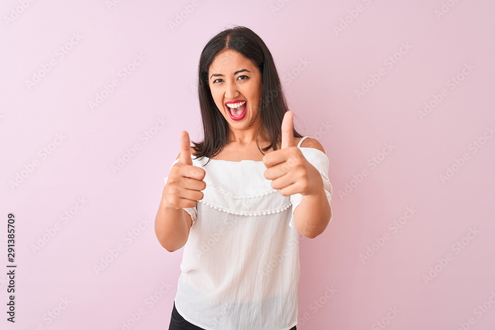 Beautiful chinese woman wearing white t-shirt standing over isolated pink background approving doing positive gesture with hand, thumbs up smiling and happy for success. Winner gesture. Beautiful chinese woman wearing white t-shirt standing over isolated pink background approving doing positive gesture with hand, thumbs up smiling and happy for success. Winner gesture.