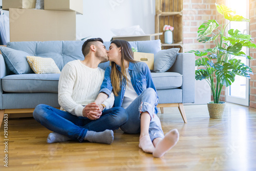 Young beautiful couple sitting on the floor of new apartment, smiling in love happy for moving to a new home