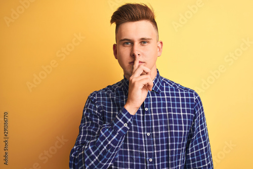 Young handsome man wearing casual shirt standing over isolated yellow background asking to be quiet with finger on lips. Silence and secret concept.
