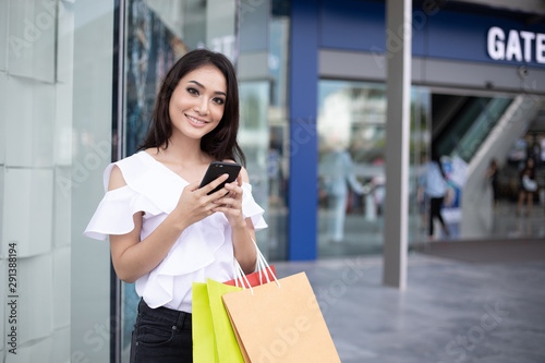 Asian women and Beautiful girl is holding shopping bags and using a smart phone and smiling while doing shopping in the supermarket/mall