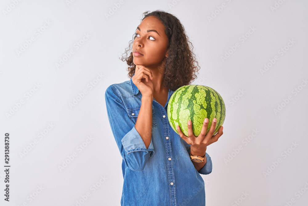 Fototapeta premium Young brazilian woman holding watermelon standing over isolated white background serious face thinking about question, very confused idea