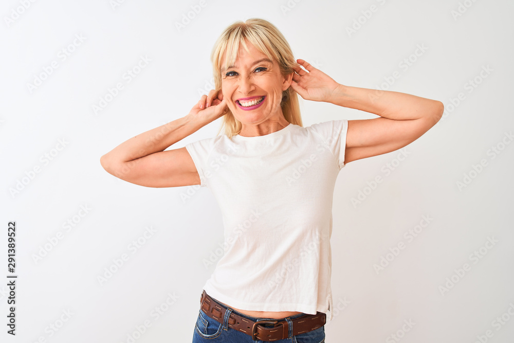 Middle age woman wearing casual t-shirt standing over isolated white background Smiling pulling ears with fingers, funny gesture. Audition problem