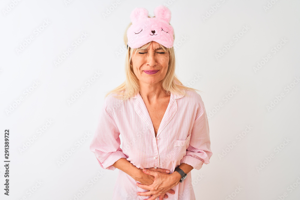 Middle age woman wearing sleep mask and pajama over isolated white background with hand on stomach because indigestion, painful illness feeling unwell. Ache concept. Middle age woman wearing sleep mask and pajama over isolated white background with hand on stomach because indigestion, painful illness feeling unwell. Ache concept.