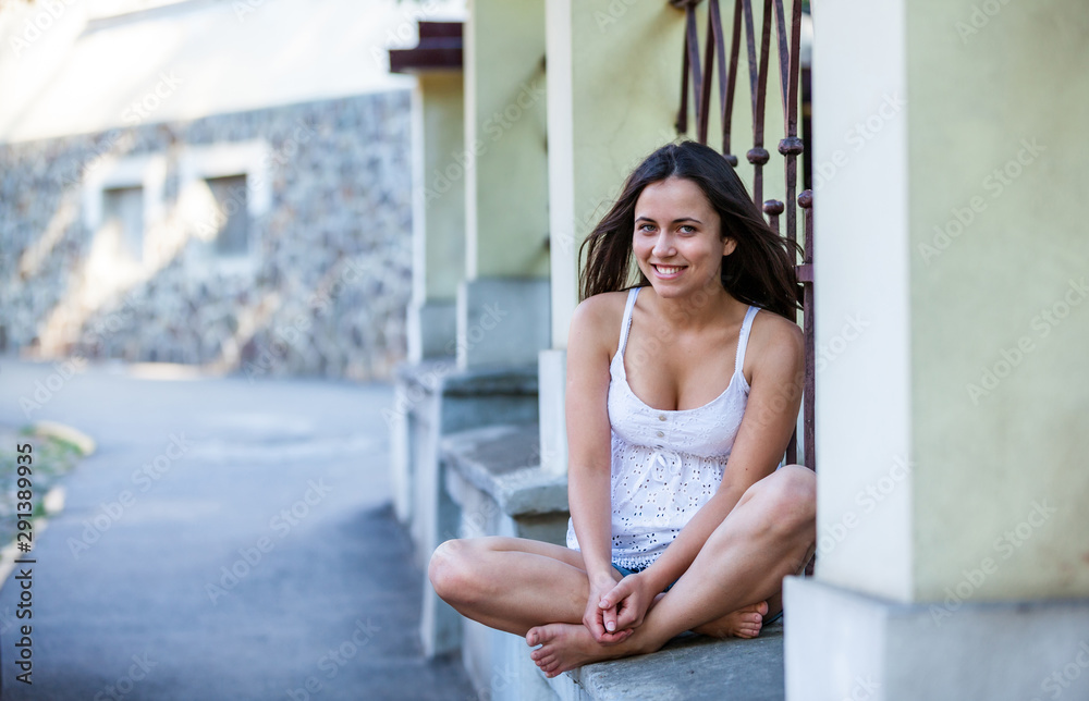 Outdoors portrait of beautiful young brunette girl sitting on street