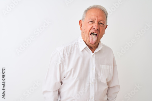 Senior grey-haired man wearing elegant shirt standing over isolated white background sticking tongue out happy with funny expression. Emotion concept.